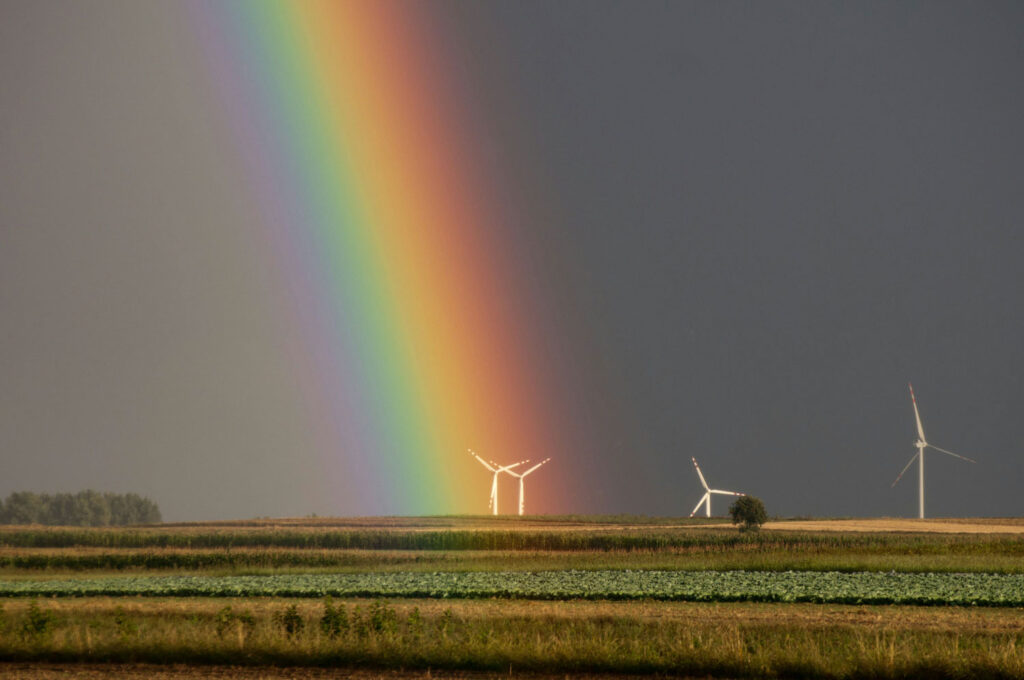 regenboog aan de hemel na slecht weer, weiland en windmolens op de achtergrond