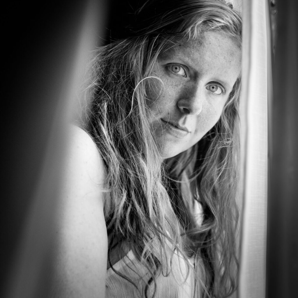 Modelfotografie in huis: model bij een raam in de slaapkamer met licht door een kier in de gordijnen