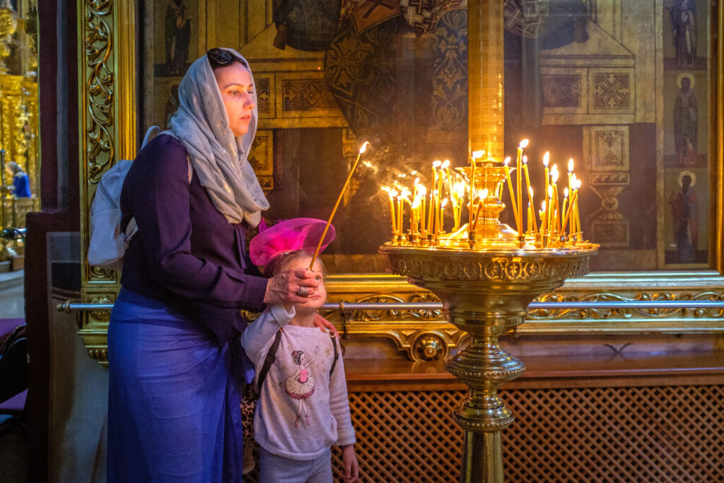 Vrouw steekt een kaars aan in een kerk, reisportret bij weinig licht