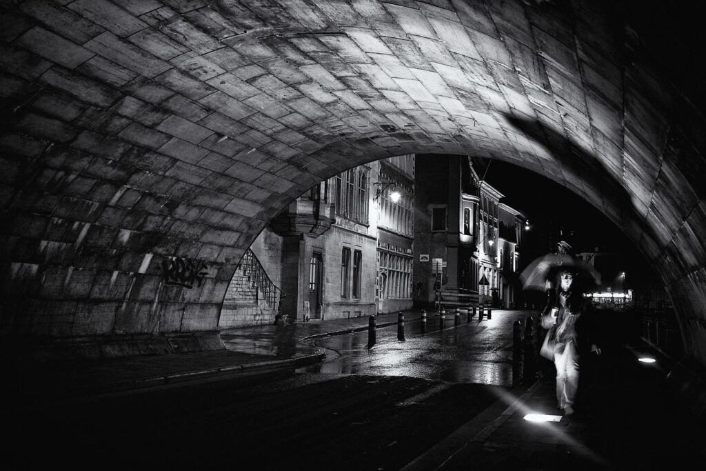 Persoon met paraplu onder een stenen brug bij nacht in Gent, sfeervol fotograferen in Gent in zwart-wit