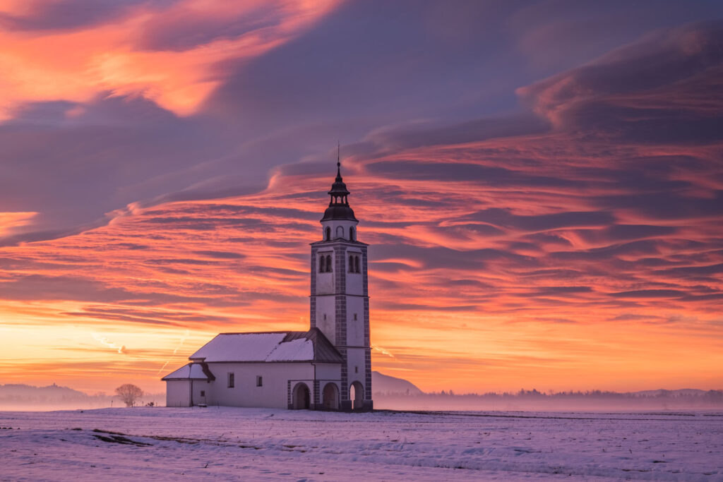 Besneeuwde kerk in Slovenië bij zonsondergang als bewerkte landschapsfoto in RAW-formaat
