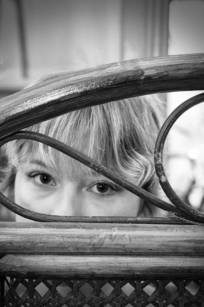 Model Yamuna kijkt door een stoel tijdens modelfotografie in zwart-wit