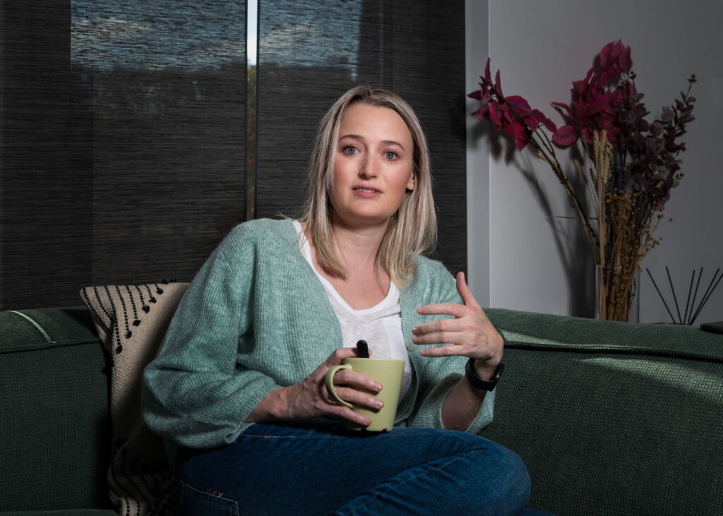 vrouw zit opgetrokken op de zetel met een kop in haar handen en vertelt haar verhaal