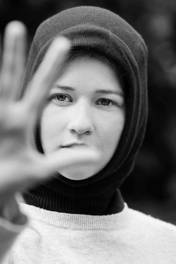 Zwart-wit portretfotografie met natuurlijk licht, model met muts en opgeheven hand voor het gezicht