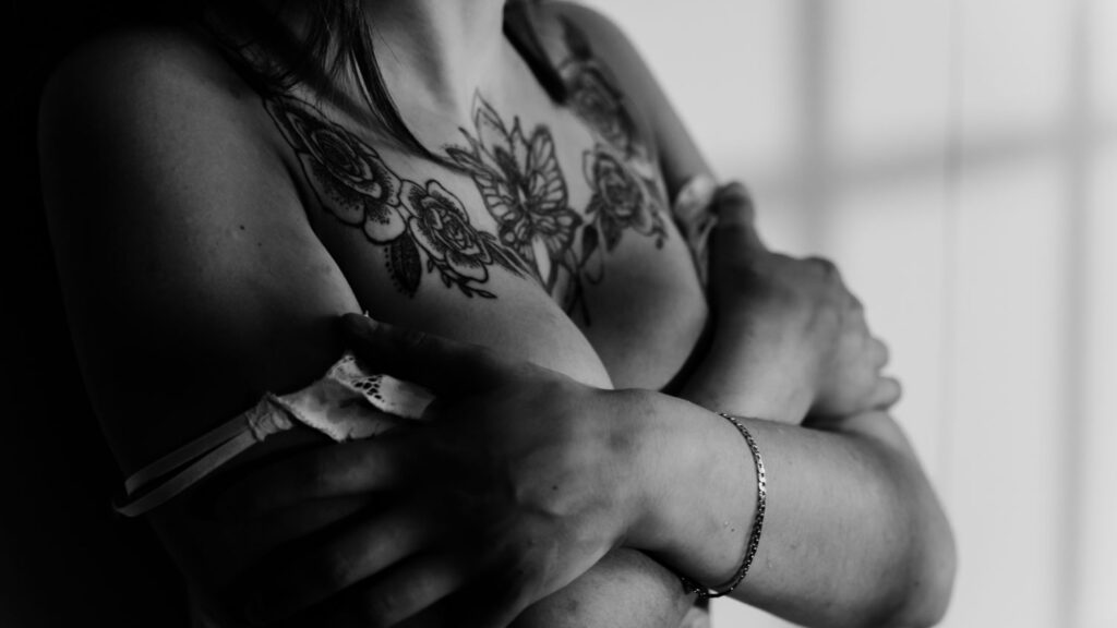 Boudoirfotografie in zwart-wit van een getatoeëerde vrouw in lingerie bij het raam