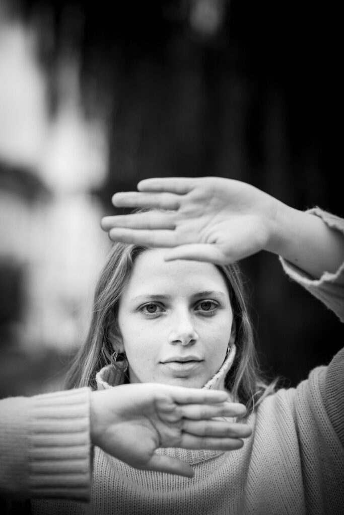 Portretfotografie met natuurlijk licht: model kadert het gezicht met beide handen in zwart-wit