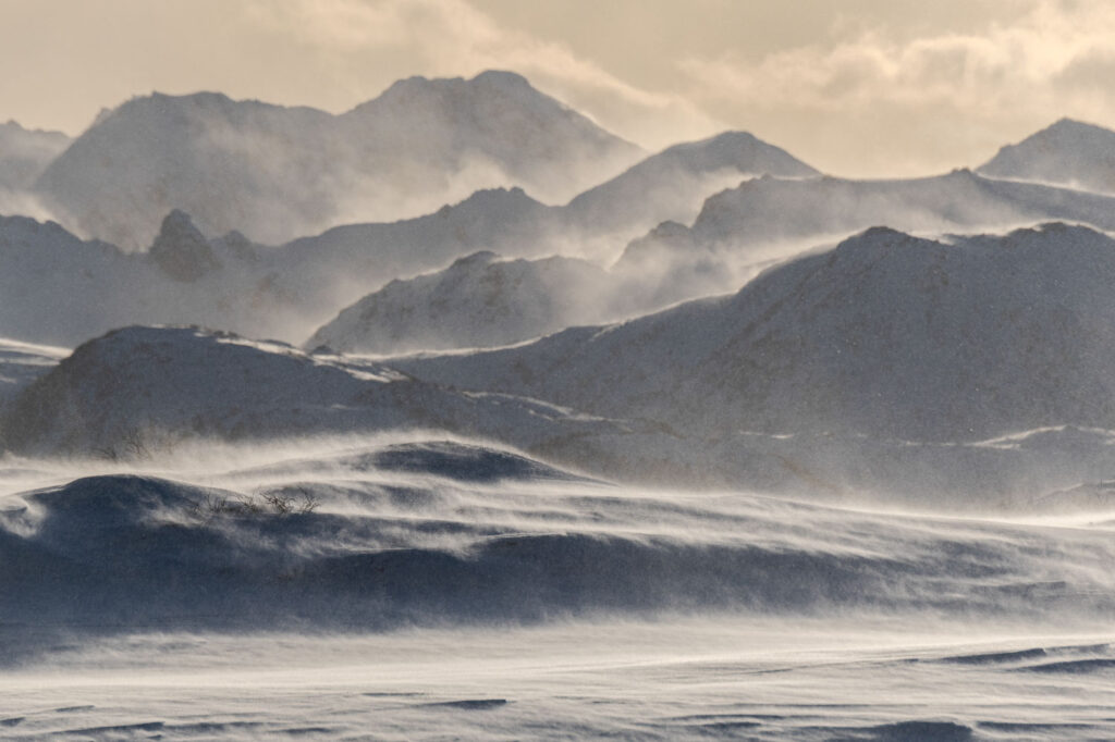 Slecht weer fotografie van een laagjeslandschap met sneeuw die langs de bergflanken opstuift