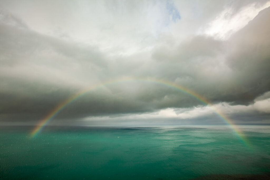 Slecht weer fotografie van een regenboog boven zee tegenover de laagstaande zon