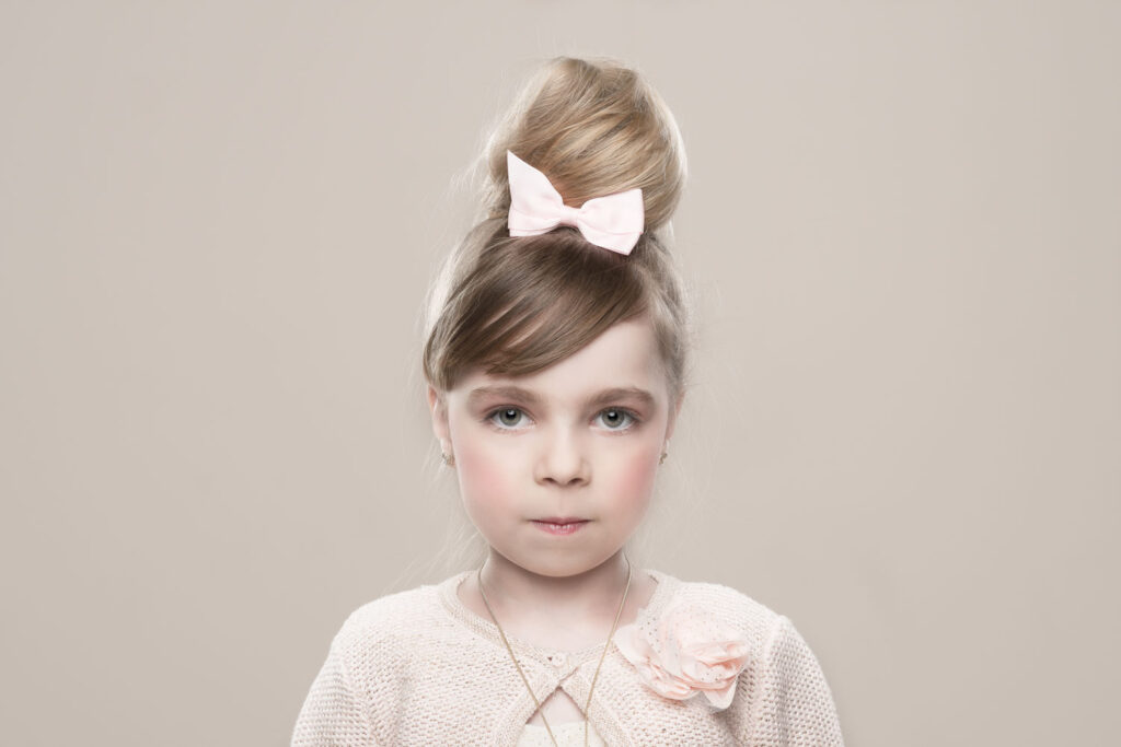 Jong meisje geportretteerd als levende porseleinen pop met lichte styling en haarstrik